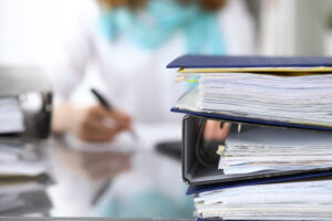 3 binders organized with stacks of papers with background blurred of woman holding pen and viewing document